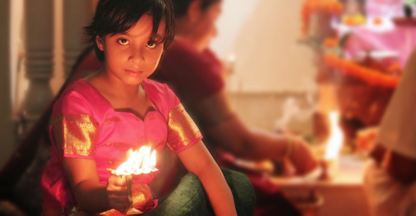 home worship image, a child holding a ghee lamp with father at the back doing deity worship at home setting.